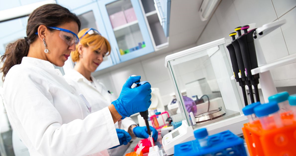 Two female scientists in white lab coats working at a laboratory bench